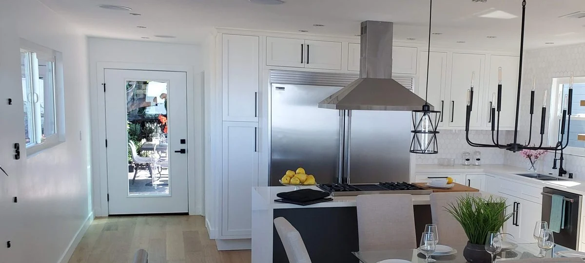Open kitchen with white shaker cabinets, an island with cooktop and a stainless range hood