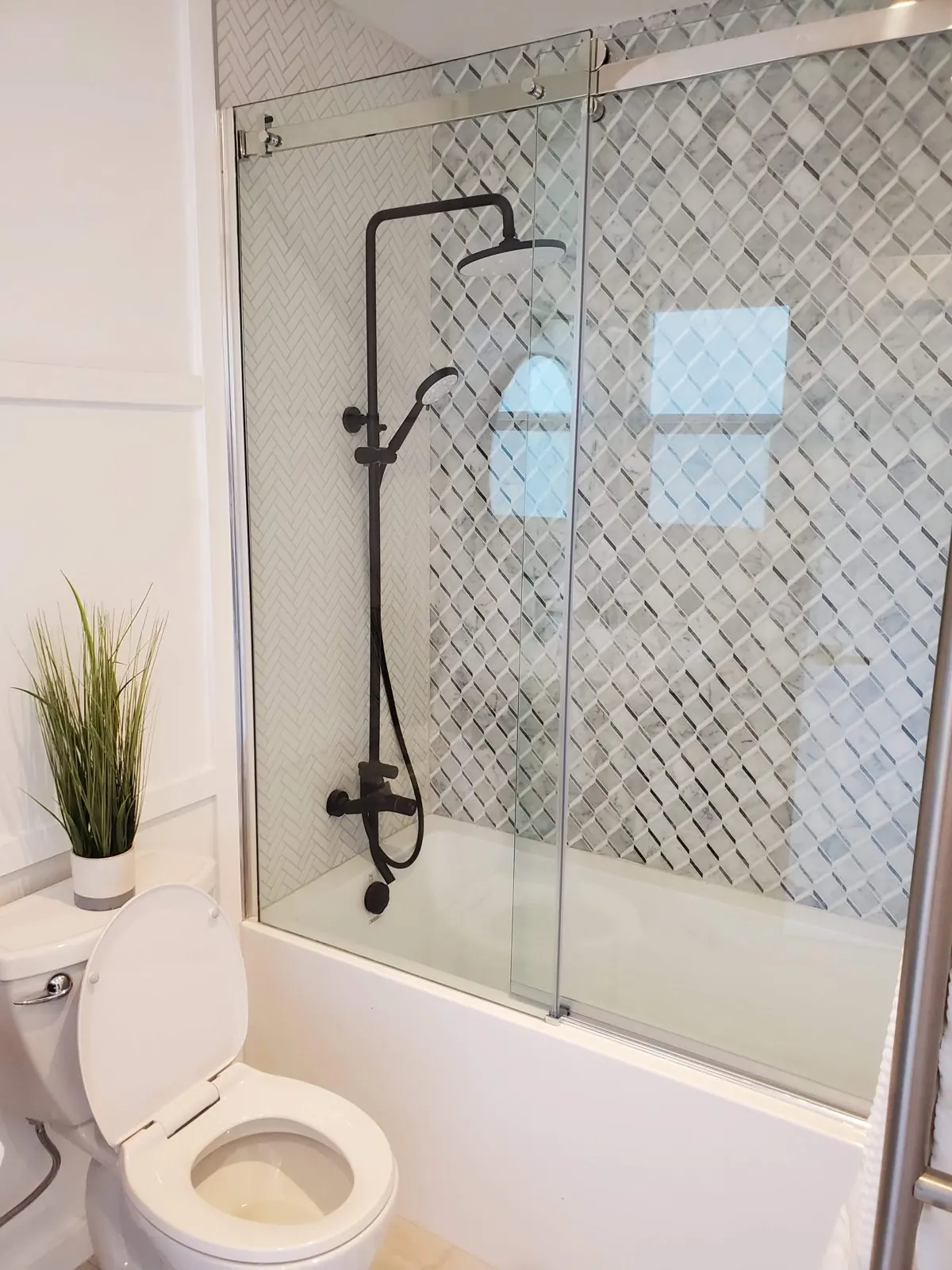 Tub and shower with a glass slider, black fixtures and marble pattern tile